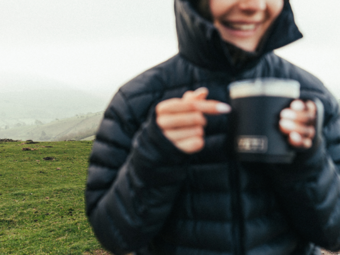 Person in a black jacket holding a coffee cup outdoors with a scenic background